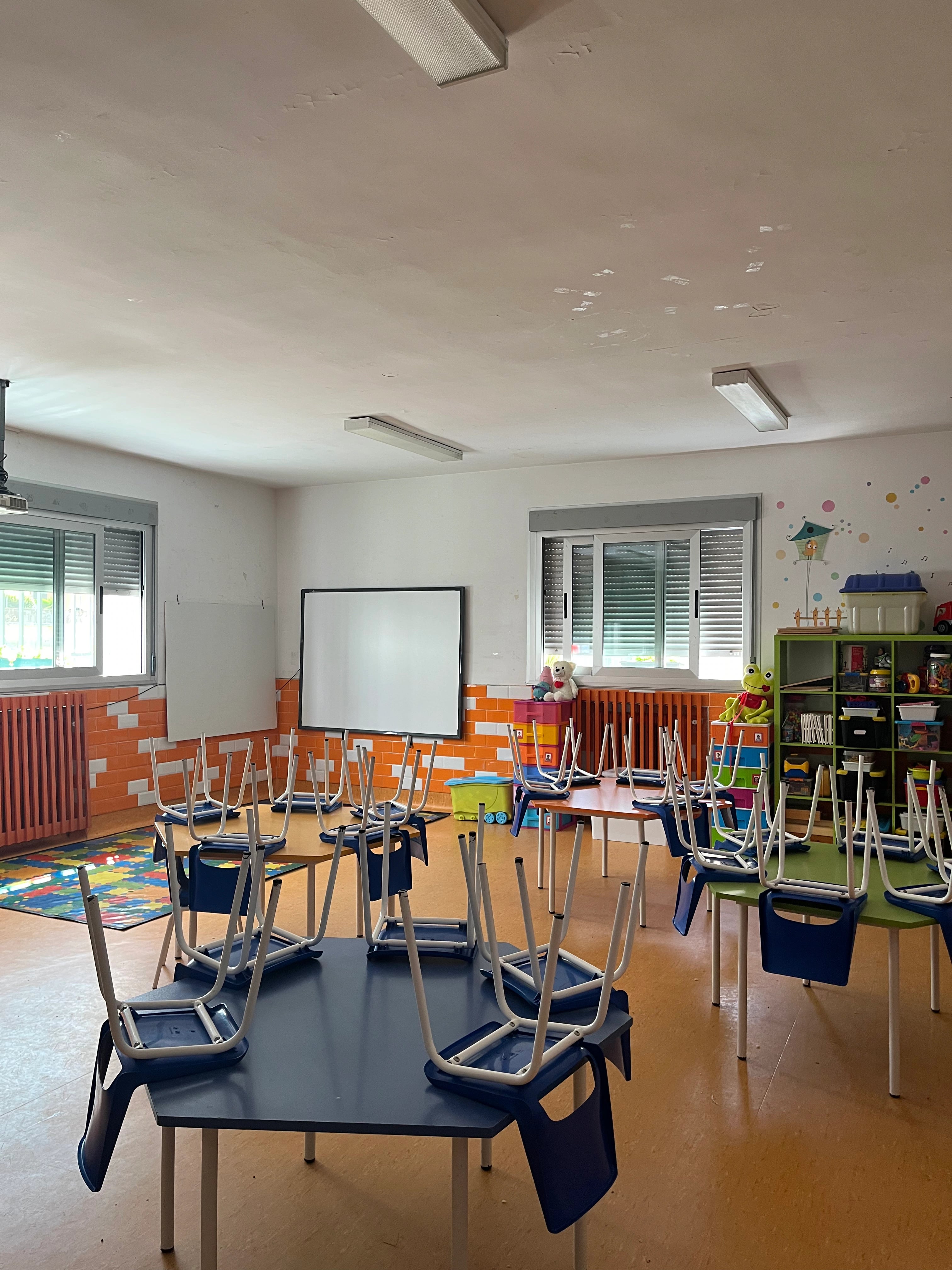 Aula de Infantil con mesas pequeñas, materiales de juego y estanterías