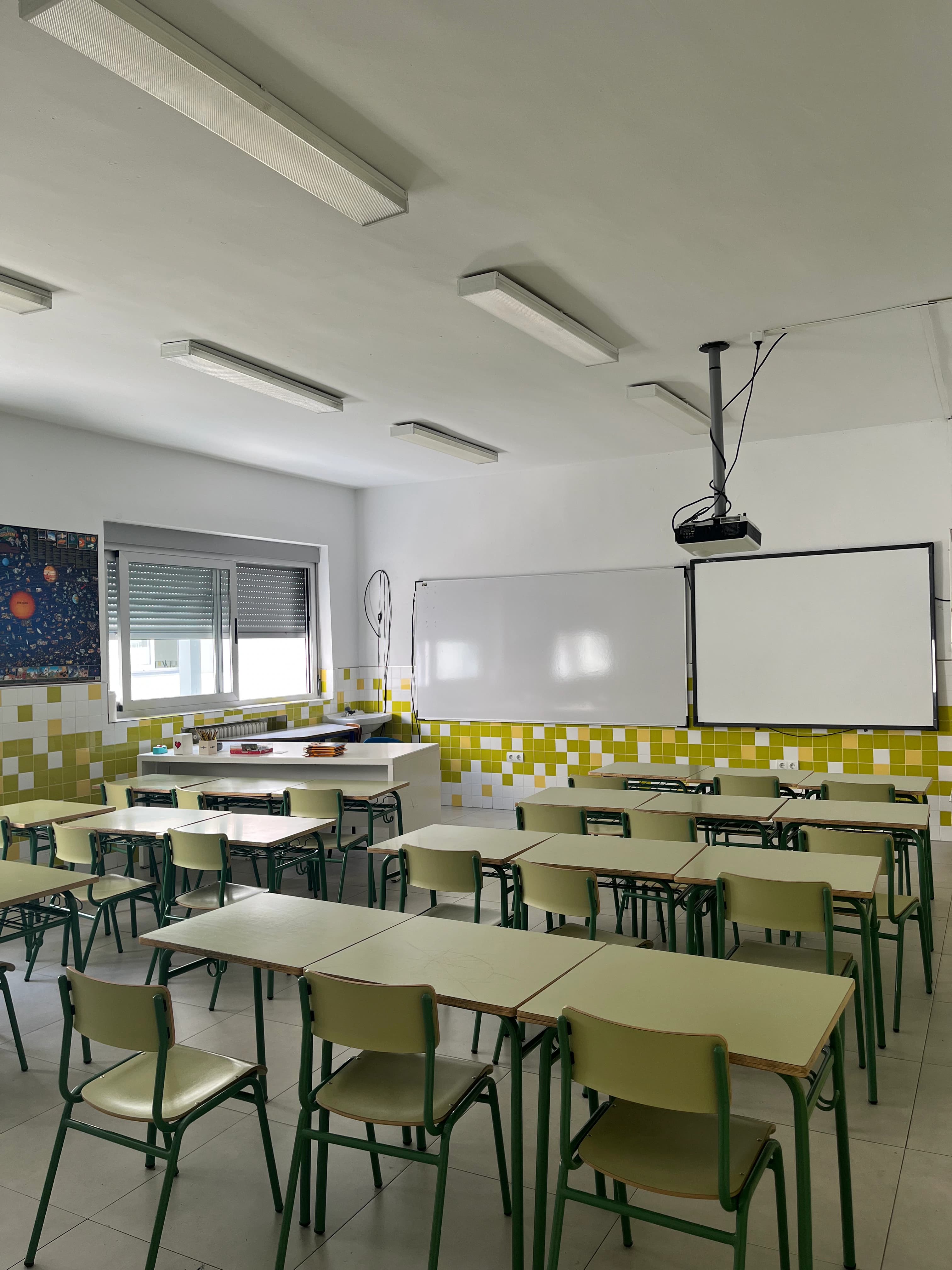 Aula del colegio con mesas verdes, pizarra y proyector