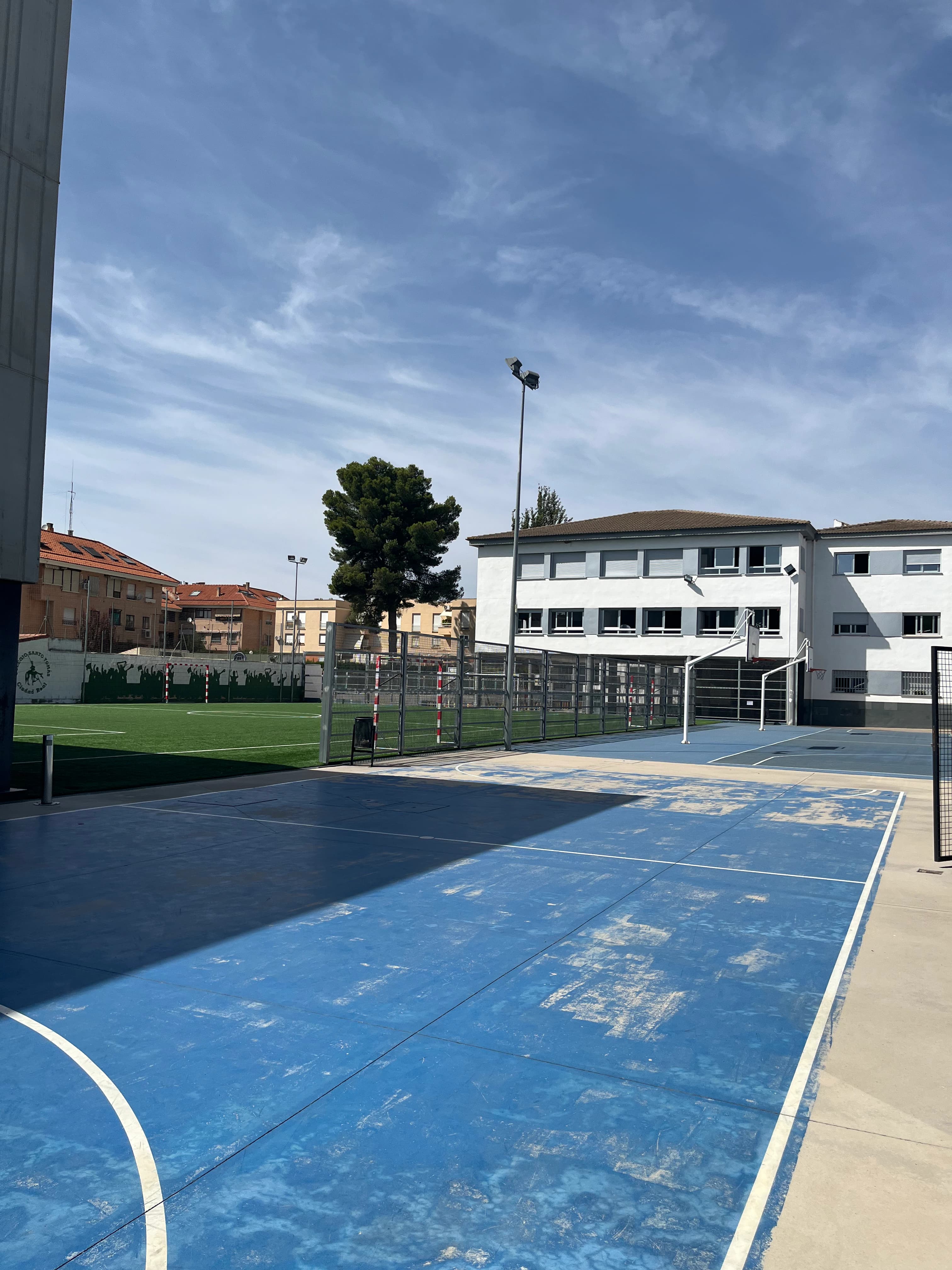 Pista azul de baloncesto con el campo de fútbol y el edificio del colegio al fondo