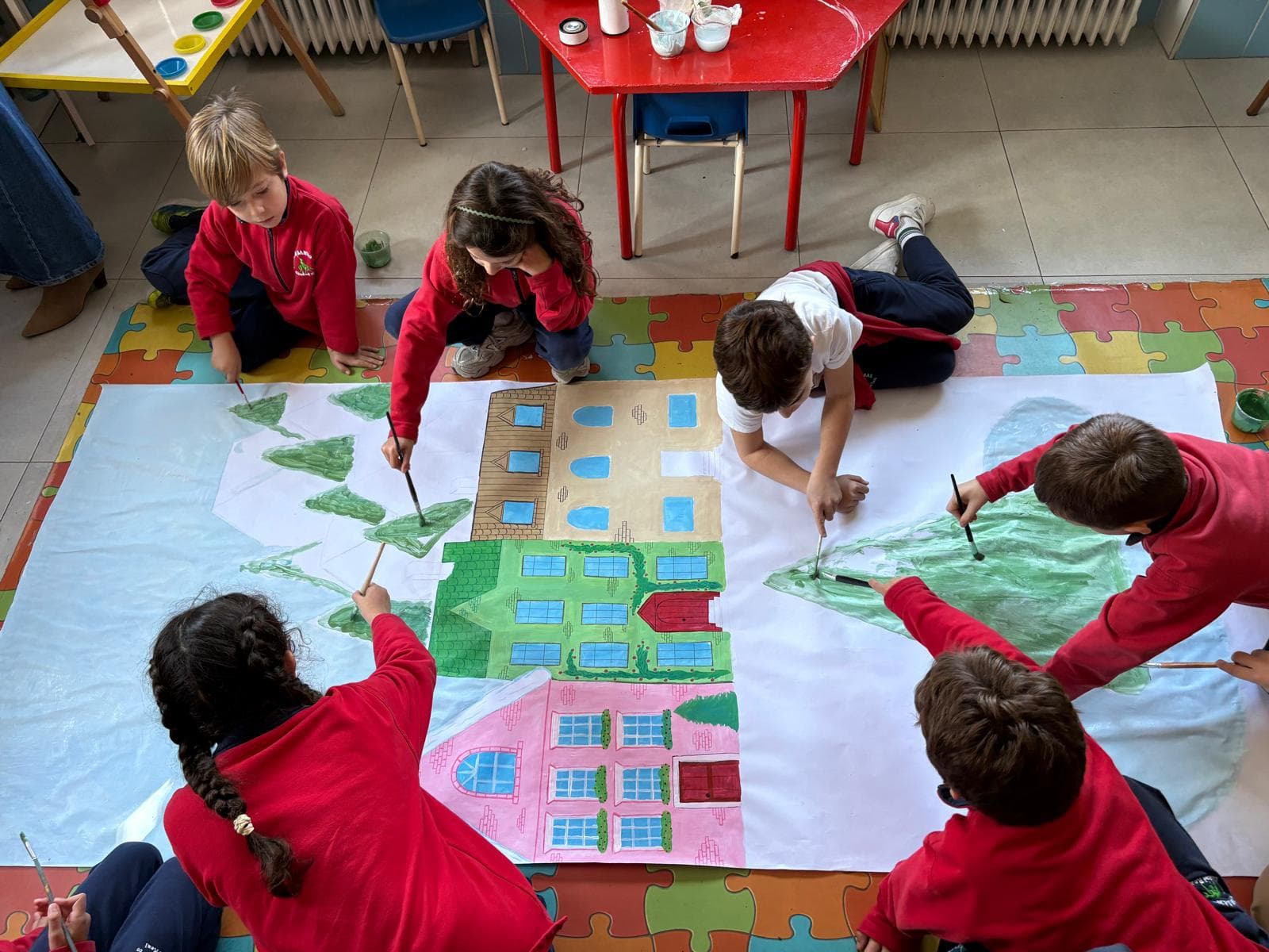 Alumnado de Santo Tomás pintando juntos un gran mural sobre el suelo del aula